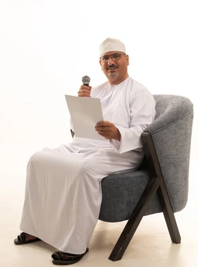 Interviews and asking questions, conducting dialogues and discussions, delivering speeches and words, exchanging dialogue and benefiting from the experiences of the elderly, a portrait of an Arab Gulf Omani man wearing a dishdasha and turban sitting on a comfortable chair holding a microphone and a white paper, full-length image, white background.