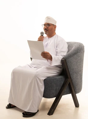 Presenting theatrical artistic performances and entertainment segments, interviews and asking questions, conducting dialogues and discussions, delivering speeches and words, a portrait of an Arab Gulf Omani man wearing a dishdasha and turban sitting on a comfortable chair holding a microphone in his hand, full-length image, white background.