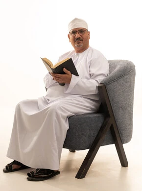 Spending time reading, learning, and gaining culture, acquiring information from books and novels, the concept of self-learning, expressions of contemplation and focus, a portrait of an elderly Arab Omani Gulf man wearing a dishdasha and kumma and reading glasses sitting on a comfortable chair reading a book, white background. Spending time reading, learning, and gaining culture, acquiring information from books and novels, the concept of self-learning, expressions of contemplation and focus, a portrait of an elderly Arab Omani Gulf man wearing a dishdasha and kumma and reading glasses sitting on a comfortable chair reading a book, white background.