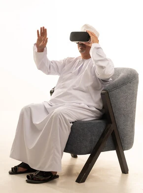Interaction and integration with holographic elements, the concept of modern electronic technologies, a portrait of an elderly Arab Saudi Gulf man sitting on a comfortable chair wearing a thobe and a headscarf, and 3D virtual reality (VR) glasses, with a white background. Interaction and integration with holographic elements, the concept of modern electronic technologies, a portrait of an elderly Arab Saudi Gulf man sitting on a comfortable chair wearing a thobe and a headscarf, and 3D virtual reality (VR) glasses, with a white background.