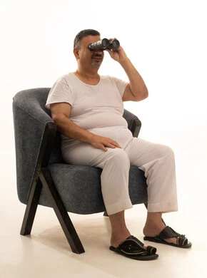 Future visions among adults and the elderly, the concept of masculinity and dignity, love for exploration and adventure, a portrait of an elderly Arab Saudi Gulf man smiling, wearing pants and a tank top and medical glasses, looking through a binocular telescope, seeing distant objects through the telescope, with a white background.