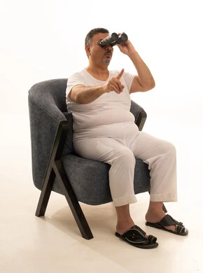 حب الاستكشاف والمغامرة، الإشارة بإصبع السبابة إلى شيء ما، رؤى مستقبلية عند الراشدين والكبار بالسن، بورتريه لرجل كبير مسن عربي سعودي خليجي مبتسم يرتدي سروال وفنيلة ونظارات طبية يقوم بالنظر من خلال المنظار ثنائي العينين(التلسكوب)، رؤية الأشياء البعيدة، خلفية بيضاء.