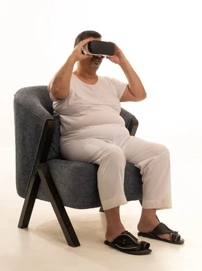 The concept of modern electronic technologies, interaction and integration with holographic elements, a portrait of an elderly Arab Saudi Gulf man sitting on a comfortable chair wearing white pants and a t-shirt, and 3D virtual reality (VR) glasses, with a white background.