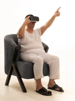Interaction and integration with holographic elements, pointing with the index finger at something, the concept of modern electronic technologies, a portrait of an elderly Arab Saudi Gulf man sitting on a comfortable chair wearing white pants and a t-shirt and 3D virtual reality (VR) glasses, white background.