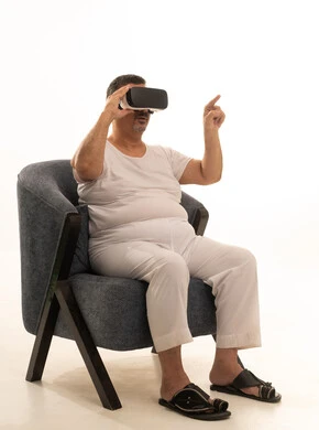 الإشارة بإصبع السبابة إلى شيء ما، التفاعل والاندماج مع العناصر الهولوجرامية، مفهوم التقنيات الإلكترونية الحديثة، بورتريه لرجل كبير بالسن عربي سعودي خليجي يجلس على كرسي مريح يرتدي السروال والفانيله البيضاء ونظارات الواقع الإفتراضي (في آر) ثلاثية الأبعاد، خلفية بيضاء