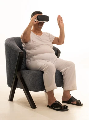 مفهوم التقنيات الإلكترونية الحديثة، التفاعل والاندماج مع العناصر الهولوجرامية، بورتريه لرجل كبير بالسن عربي سعودي خليجي يجلس على كرسي مريح يرتدي السروال والفانيله البيضاء ونظارات الواقع الإفتراضي (في آر) ثلاثية الأبعاد، خلفية بيضاء