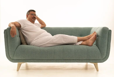 Looking at something, gestures of thinking, boredom, and annoyance, spending free time in contemplation, a portrait of an elderly Arab Saudi Gulf man wearing pants and a t-shirt, wearing reading glasses, reclining on a comfortable sofa with his hand behind his head, white background.