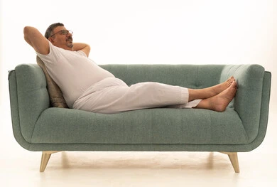 إيماءات التفكير والملل والضجر، قضاء وقت الفراغ بالتأمل، بورتريه لرجل كبير بالسن عربي سعودي خليجي يرتدي سروال و فانيلة ويضع نظارات طبية يستلقي على اريكة مريحة ويضع يديه خلف رأسه، خلفية بيضاء