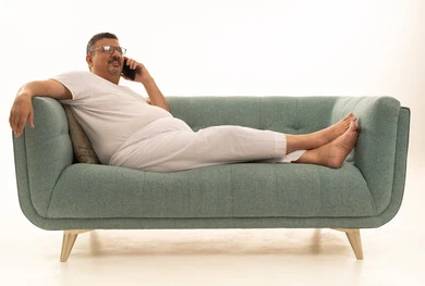 Making a phone call via mobile, a modern and advanced technical device, a portrait of an elderly Arab Saudi Gulf man wearing pants and a t-shirt and wearing reading glasses sitting on a comfortable sofa using a mobile phone, white background.