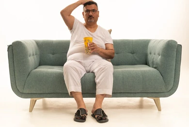 ايماءات الصدمة و الزهول، قضاء وقت الفراغ بمتابعة الافلام و المسلسلات المسلية،تناول سناك صحي و خفيف ، بورتريه لرجل كبير السن عربي خليجي سعودي يرتدي سروال وفنيله ونظارات طبية يجلس على اريكه مريحة ويقوم بتناول الفشار، خلفية بيضاء