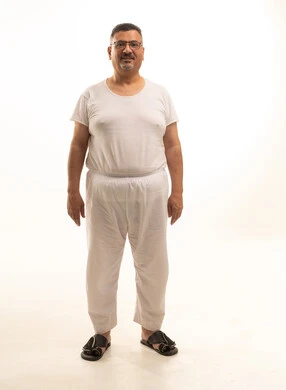 الوقوف باستقامة و النظر الى الكاميرا بايماءات الجدية والثقة بالنفس، بورتريه لرجل كبير السن عربي خليجي سعودي يرتدي سروال وفنيله ونظارات طبية ، الجسم بالطول الكامل، خلفية بيضاء