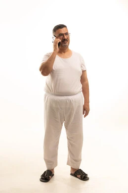 Making a phone call via mobile, a modern and advanced technical device, communicating with family and friends, a portrait of an elderly Arab Saudi Gulf man wearing pants and a t-shirt and wearing reading glasses using a mobile phone, full body, white background.