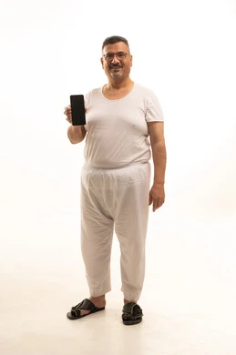 عرض شاشة سوداء فارغة عبر الجوال، جهاز تقني حديث ومتطور، انظر إلى الكاميرا بإيماءات السرور، بورتريه لرجل كبير بالسن عربي سعودي خليجي يرتدي سروال و فانيلة ويضع نظارات طبية يقوم باستخدام الهاتف المحمول، الجسم بالطول الكامل، خلفية بيضاء