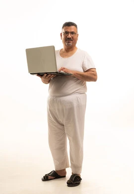 تصفح مواقع الانترنت، جهاز تقني حديث ومتطور، إنجاز مهام العمل عن بعد، بورتريه لرجل كبير بالسن عربي سعودي خليجي يرتدي سروال و فانيلة ويضع نظارات طبية يقوم باستخدام الحاسوب المحمول، الجسم بالطول الكامل، خلفية بيضاء