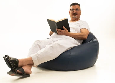 تعابير التمعن والتركيز، قضاء الوقت بالقراءة والتعلم والثقافة، مفهوم التعلم الذاتي، بورتريه لرجل كبير بالسن عربي سعودي خليجي يرتدي سروال و فانيلة  يجلس على كرسي بين باج مريح يقوم بمطالعة كتاب، خلفية بيضاء