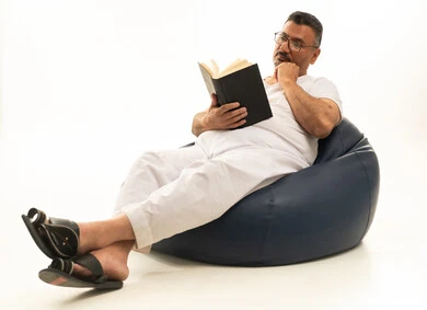 مفهوم التعلم الذاتي، تعابير التمعن والتركيز، قضاء الوقت بالقراءة والتعلم والثقافة،  بورتريه لرجل كبير بالسن عربي سعودي خليجي يرتدي سروال و فانيلة  يجلس على كرسي بين باج مريح يقوم بمطالعة كتاب، خلفية بيضاء