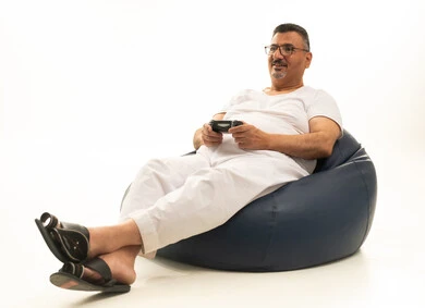 قضاء وقت ممتع ومسلي، تقنيات حديثة مسلية, التفاعل والاندماج مع ألعاب البلايستيشن، بورتريه لرجل كبير بالسن عربي سعودي خليجي يرتدي سروال وفانيلة بيضاء يجلس على كرسي مريح يحمل بيده عصا التحكم  ويلعب بألعاب الفيديو، خلفية بيضاء