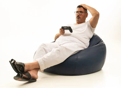 تعابير وايماءات الخسارة ، قضاء وقت ممتع ومسلي، تقنيات حديثة مسلية, التفاعل والاندماج مع ألعاب البلايستيشن، بورتريه لرجل كبير بالسن عربي سعودي خليجي يرتدي سروال وفانيلة بيضاء يجلس على كرسي مريح يحمل بيده عصا التحكم  ويلعب بألعاب الفيديو، خلفية بيضاء