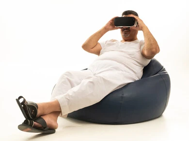 تعابير التفاعل والاندماج مع العناصر الهولوجرامية، مفهوم التقنيات الإلكترونية الحديثة، بورتريه لرجل كبير بالسن عربي سعودي خليجي يجلس على كرسي مريح يرتدي السروال والفانيله البيضاء ونظارات الواقع الإفتراضي (في آر) ثلاثية الأبعاد، خلفية بيضاء