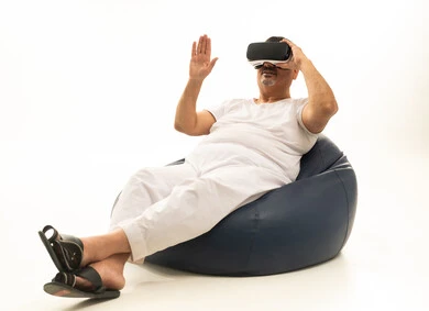 The concept of modern electronic technologies, gestures of interaction and integration with holographic elements, a portrait of an elderly Arab Saudi Gulf man sitting on a comfortable chair wearing white pants and a tank top, and 3D virtual reality (VR) glasses, with a white background.