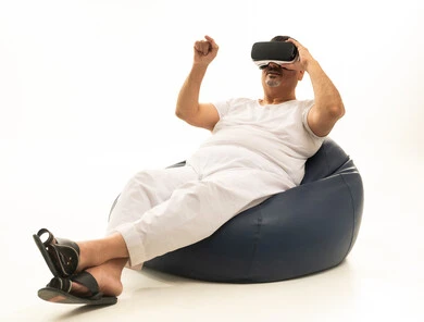 Gestures of interaction and integration with holographic elements, the concept of modern electronic technologies, a portrait of an elderly Arab Saudi Gulf man sitting on a comfortable chair wearing white pants and a tank top, and 3D virtual reality (VR) glasses, white background.