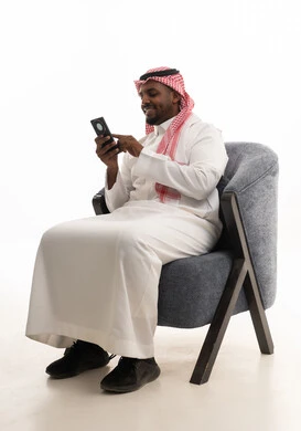 Integrating modern technologies into daily life, using a mobile phone, making a phone call with family and friends, browsing social media, a portrait of a Saudi Arabian Gulf man wearing traditional attire and a ghutrah holding a mobile phone in his hand, white background.