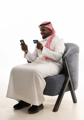 التسويق اونلاين عبر الانترنت ، الدفع عبر بطاقة الائتمان ، بورتريه لرجل عربي خليجي سعودي يرتدي الثوب التقليدي والشماغ يمسك الجوال والبطاقة بيده ،دمج التقنيات الحديثة فى الحياة اليومية ، خلفية بيضاء