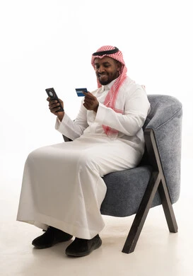 الدفع عبر بطاقة الائتمان ، التسويق اونلاين عبر الانترنت ، بورتريه لرجل عربي خليجي سعودي يرتدي الثوب التقليدي والشماغ يمسك الجوال والبطاقة بيده ،دمج التقنيات الحديثة فى الحياة اليومية ، خلفية بيضاء
