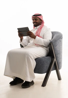 دمج التقنيات الحديثة فى الحياة اليومية ، استخدام الجهاز اللوحي  ، إجراء بث مباشر مع الأهل والأصدقاء، تصفح مواقع التواصل الاجتماعي ، بورتريه لرجل عربي خليجي سعودي يرتدي الثوب التقليدي والشماغ يمسك جهاز التابلت بيده ، خلفية بيضاء