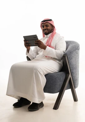 Browsing social media, a portrait of a Saudi Arabian Gulf man wearing traditional attire and a ghutrah holding a tablet in his hand, integrating modern technologies into daily life, using the tablet, conducting a live broadcast with family and friends, white background.