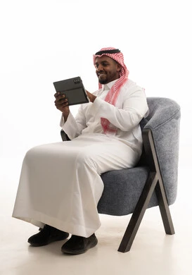 إجراء بث مباشر مع الأهل والأصدقاء، تصفح مواقع التواصل الاجتماعي ، دمج التقنيات الحديثة فى الحياة اليومية ، استخدام الجهاز اللوحي  ،بورتريه لرجل عربي خليجي سعودي يرتدي الثوب التقليدي والشماغ يمسك جهاز التابلت بيده ، خلفية بيضاء