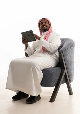استخدام الجهاز اللوحي  ، إجراء بث مباشر مع الأهل والأصدقاء،دمج التقنيات الحديثة فى الحياة اليومية ، تصفح مواقع التواصل الاجتماعي ، بورتريه لرجل عربي خليجي سعودي يرتدي الثوب التقليدي والشماغ يمسك جهاز التابلت بيده ، خلفية بيضاء