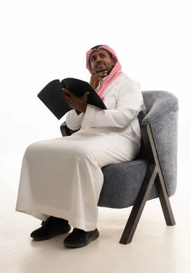 حب المطالعة والقراءة ،تمضية أوقات الفراغ بالتعلم والتثقف الذاتي, إيماءات التأمل والتفكير، بورتريه لرجل عربي خليجي سعودي يرتدي الثوب التقليدي والشماغ يجلس على مكتب يقوم بقراءه كتاب   ، خلفية بيضاء