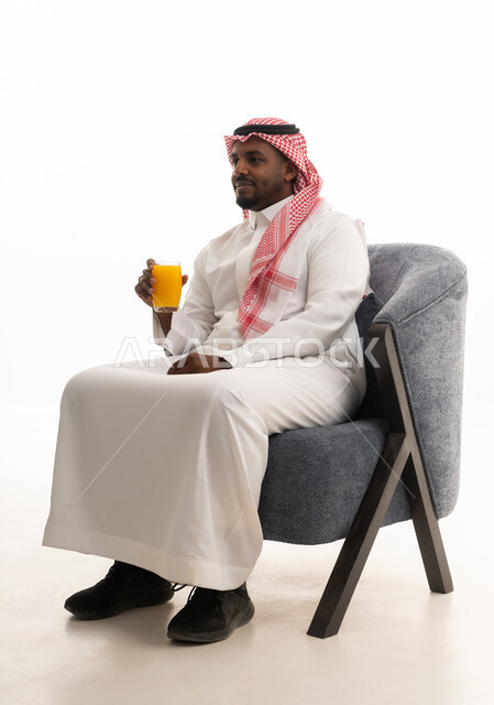 بورتريه لرجل عربي خليجي سعودي يرتدي الزي التقليدي والشماغ يستمتع بشرب العصير الطبيعي البارد، محاولة التخفيف من حرارة الصيف بالعصائر المنعشة، الاستمتاع بتناول المشروبات المفيدة اللذيذة، خلفية بيضاء