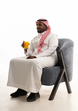 A portrait of a Saudi Arabian Gulf man wearing traditional attire and a ghutrah, enjoying a cold natural juice, trying to alleviate the summer heat with refreshing juices, enjoying delicious and beneficial drinks, with a white background.
