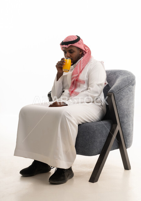 Trying to alleviate the summer heat with refreshing juices, enjoying delicious and beneficial drinks, a portrait of an Arab Gulf Saudi man wearing traditional attire and a ghutrah enjoying a cold natural juice, with a white background.