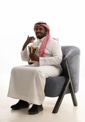 استخدام خشب العود بالأعياد والمناسبات, العادات والتقاليد السعودية, بورتريه لرجل عربي خليجي سعودي يرتدي الثوب التقليدي والشماغ  يجلس على كرسي مريح يقوم بالتعطر من المبخرة, الاهتمام بالمظهر الخارجي والأناقة, التعطر والتطيب بالبخور, خلفية بيضاء