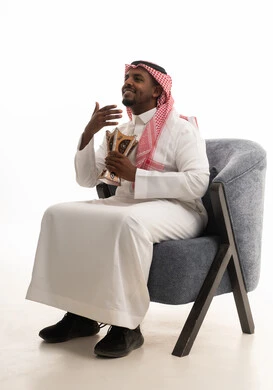 التعطر والتطيب بالبخور, استخدام خشب العود بالأعياد والمناسبات, العادات والتقاليد السعودية, بورتريه لرجل عربي خليجي سعودي يرتدي الثوب التقليدي والشماغ  يجلس على كرسي مريح يقوم بالتعطر من المبخرة, الاهتمام بالمظهر الخارجي والأناقة, خلفية بيضاء