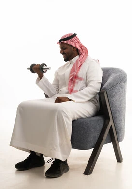 بورتريه لرجل عربي خليجي سعودي مبتسم يرتدي الشماغ والثوب التقليدي يقوم برفع الأوزان الحديدية الثقيلة، المحافظة على الصحة واللياقة الجسدية، تمارين رفع الأثقال (دمبلز)، ممارسة التمارين الرياضية مع الدمبل، خلفية بيضاء