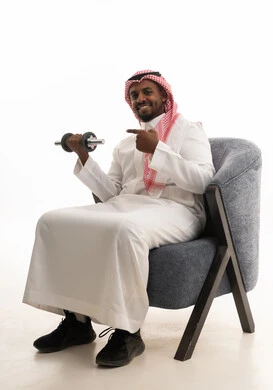 تمارين رفع الأثقال (دمبلز)، ممارسة التمارين الرياضية مع الدمبل، بورتريه لرجل عربي خليجي سعودي مبتسم يرتدي الشماغ والثوب التقليدي يقوم برفع الأوزان الحديدية الثقيلة، المحافظة على الصحة واللياقة الجسدية، خلفية بيضاء