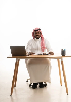 بورتريه لرجل عربي خليجي سعودي يرتدي الثوب التقليدي والشماغ يجلس على مكتب يستخدم الحاسوب المحمول ، حب المطالعة والقراءة ،تمضية أوقات الفراغ بالتعلم والتثقف الذاتي, إيماءات الانتباه والتركيز،دمج التقنيات الحديثة فى الحياة اليومية ، إجراء بث مباشر مع الأهل والأصدقاء، اجتماع عمل عن بعد، خلفية بيضاء
