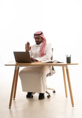Making video calls with family and friends, a remote work meeting, a portrait of a Saudi Arabian Gulf man wearing traditional attire and a ghutrah sitting at a desk holding a tablet looking at it with gestures of happiness, white background.