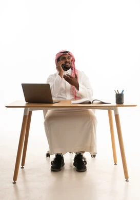 اجتماع عمل عن بعد، بورتريه لرجل عربي خليجي سعودي يرتدي الثوب التقليدي والشماغ يمسك الجوال بيده يستخدم الحاسوب المحمول ، دمج التقنيات الحديثة فى الحياة اليومية ، استخدام الهاتف المحمول ، إجراء بث مباشر مع الأهل والأصدقاء،خلفية بيضاء
