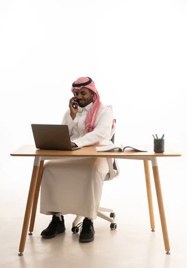 استخدام الهاتف المحمول ، دمج التقنيات الحديثة فى الحياة اليومية ، إجراء بث مباشر مع الأهل والأصدقاء، اجتماع عمل عن بعد، بورتريه لرجل عربي خليجي سعودي يرتدي الثوب التقليدي والشماغ يمسك الجوال بيده يستخدم الحاسوب المحمول ، خلفية بيضاء