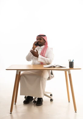 دمج التقنيات الحديثة فى الحياة اليومية ، استخدام الهاتف المحمول ، إجراء بث مباشر مع الأهل والأصدقاء، تصفح مواقع التواصل الاجتماعي ، بورتريه لرجل عربي خليجي سعودي يرتدي الثوب التقليدي والشماغ يمسك الجوال بيده  وامامه كتاب ، خلفية بيضاء