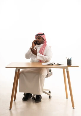 استخدام الهاتف المحمول ، إجراء بث مباشر مع الأهل والأصدقاء، دمج التقنيات الحديثة فى الحياة اليومية ،تصفح مواقع التواصل الاجتماعي ، بورتريه لرجل عربي خليجي سعودي يرتدي الثوب التقليدي والشماغ يمسك الجوال بيده  وامامه كتاب ، خلفية بيضاء