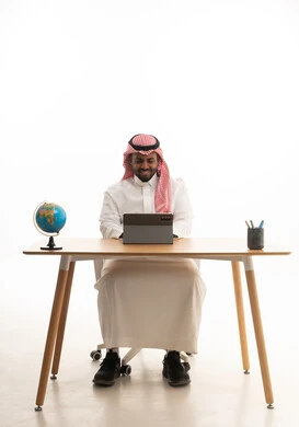 بورتريه لرجل عربي خليجي سعودي يرتدي الثوب التقليدي والشماغ يجلس على مكتب يمسك جهاز التابلت ينظر بإيماءات السعادة، إجراء مكالمات الفيديو مع الأهل والأصدقاء، اجتماع عمل عن بعد، خلفية بيضاء