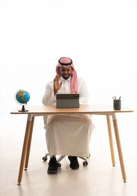 تعابير الترحيب والتعارف ،اجتماع عمل عن بعد، إجراء مكالمات الفيديو مع الأهل والأصدقاء،بورتريه لرجل عربي خليجي سعودي يرتدي الثوب التقليدي والشماغ يجلس على مكتب يمسك جهاز التابلت ينظر بإيماءات السعادة، خلفية بيضاء