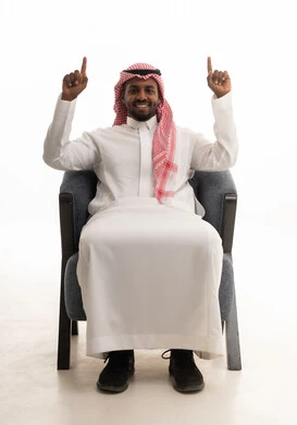 النظر الى الكاميرا بايماءات السعادة والسرور، تحديد موقع معين، الإشارة والتوضيح إلى شيء ما، بورتريه لرجل عربي خليجي سعودي يرتدي الثوب التقليدي والشماغ يرفع اصبعي السبابة إلى الأعلى،  خلفية بيضاء