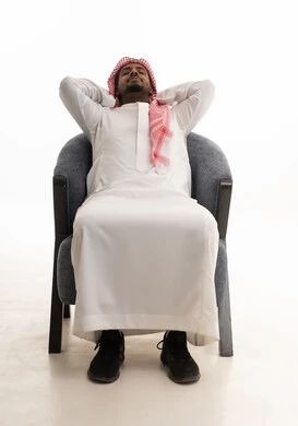 تعابير التأمل والتفكير، الحاجة إلى النوم والشعور بالتعب و الخمول, بورتريه لرجل عربي خليجي سعودي يرتدي الثوب التقليدي والشماغ يجلس على كرسي مريح يضع يديه خلف راسه بإيماءات الراحة والإسترخاء, خلفية بيضاء.